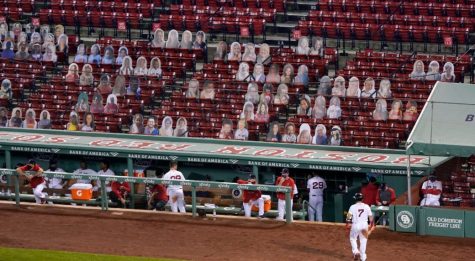 Boston Redsox player walks back to dugout as cardboard fans look on. These cut outs have replaced many of the fans in stadiums now.